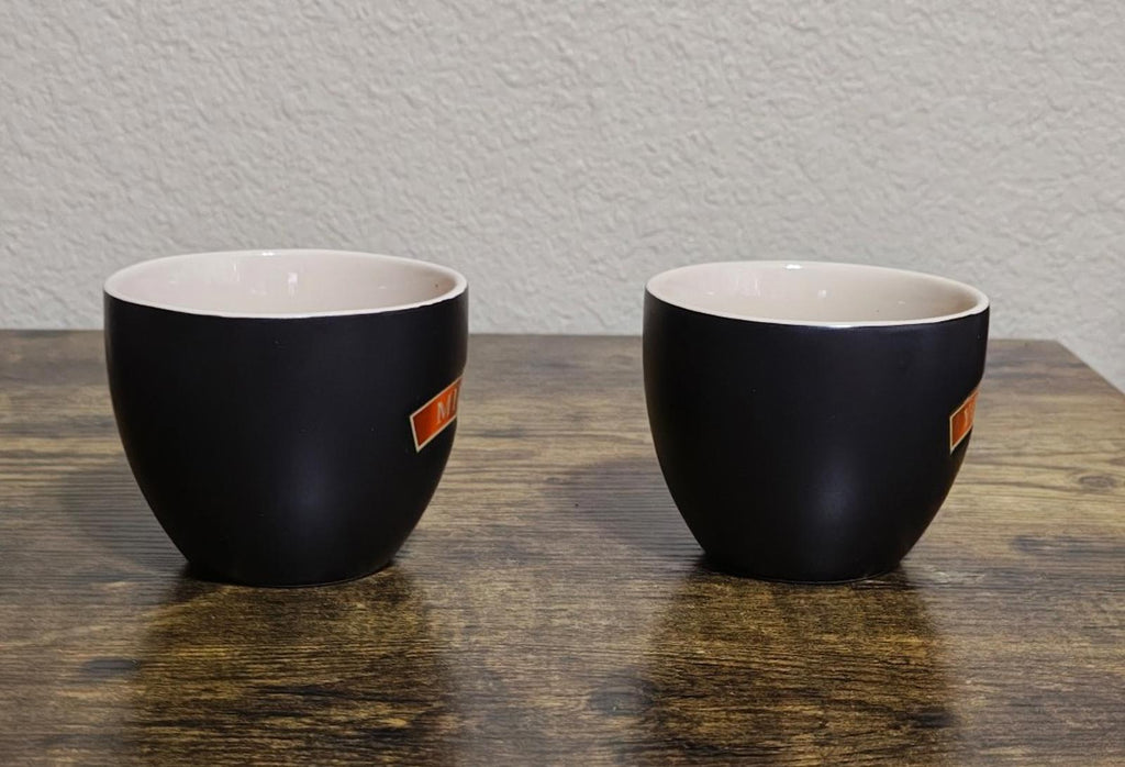Black stoneware cups with partial orange 'Mine' and 'Yours' badges