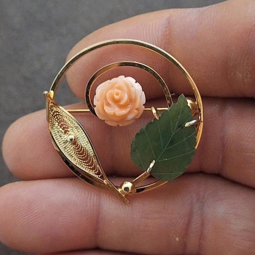 Gold-tone filigree brooch with pale rose and green leaf accents on a circular frame.