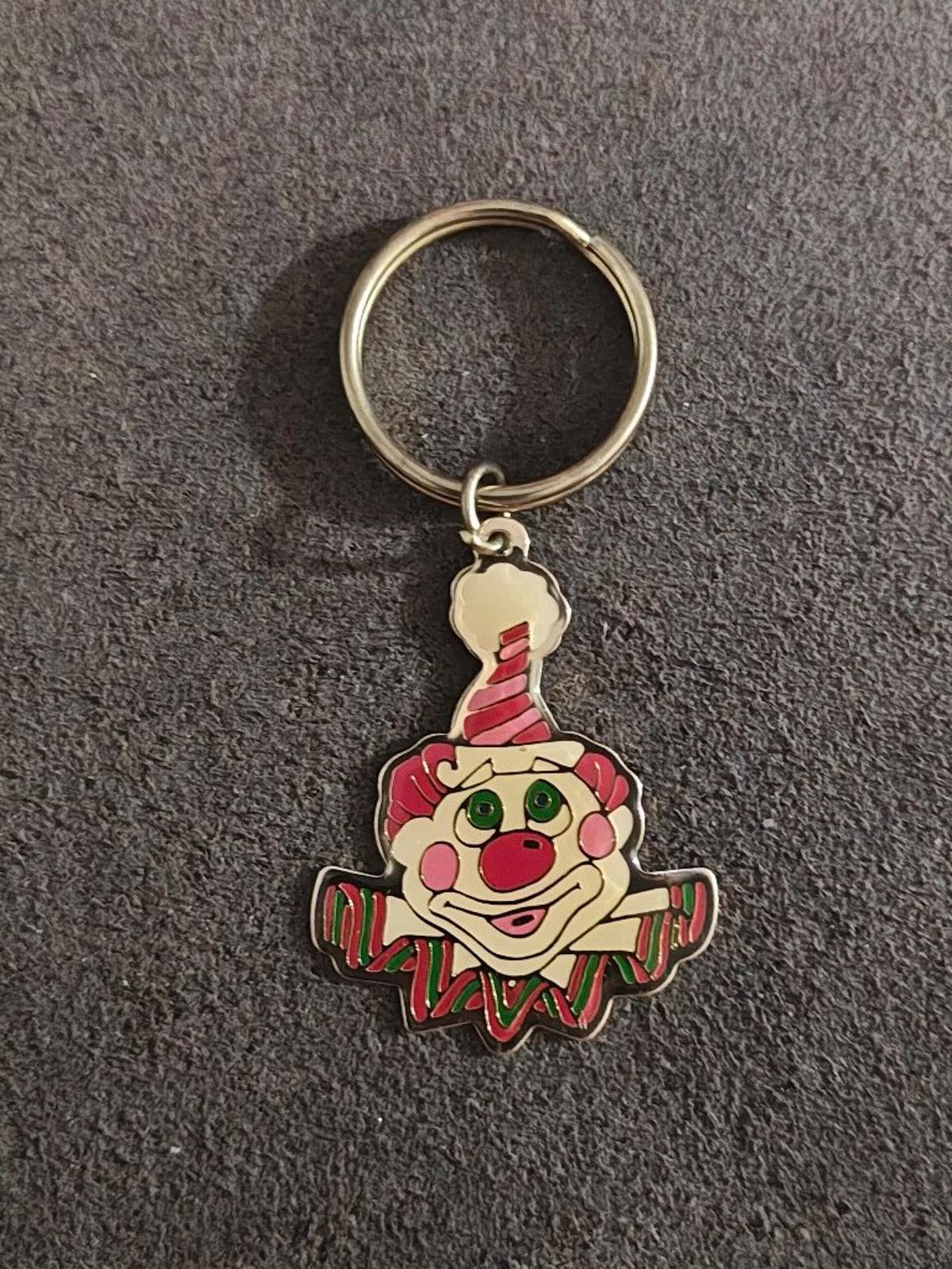 Gold-tone clown keychain with ring and multicolor clown face charm on dark carpet