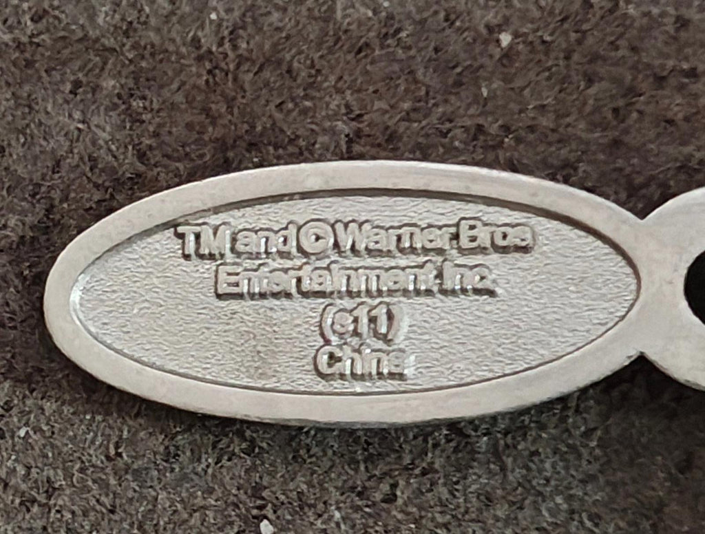 Close-up oval metal charm tag with engraved Universal and Warner Bros. text