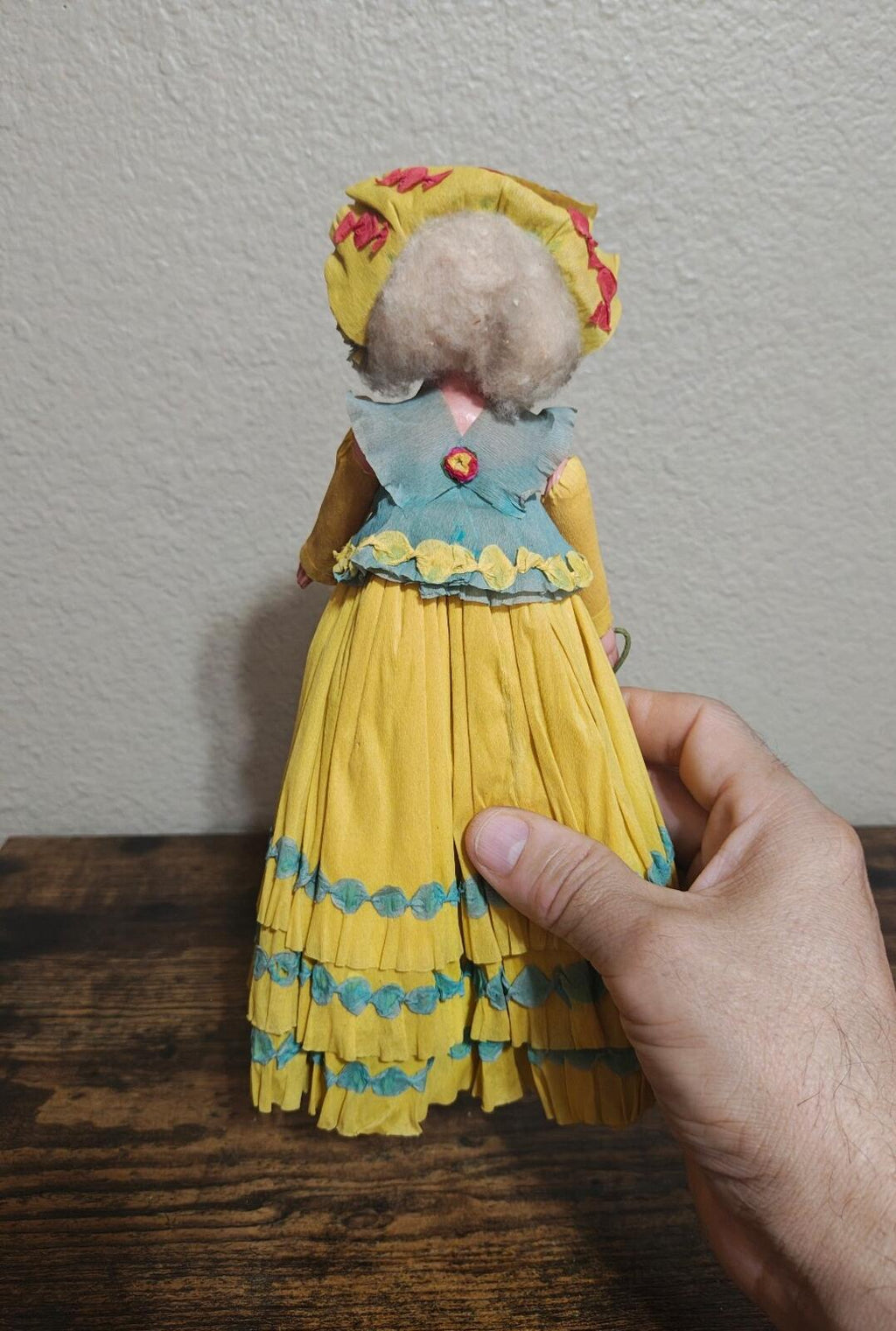 Handcrafted crepe paper doll in yellow dress with blue layered hem and bonnet detail