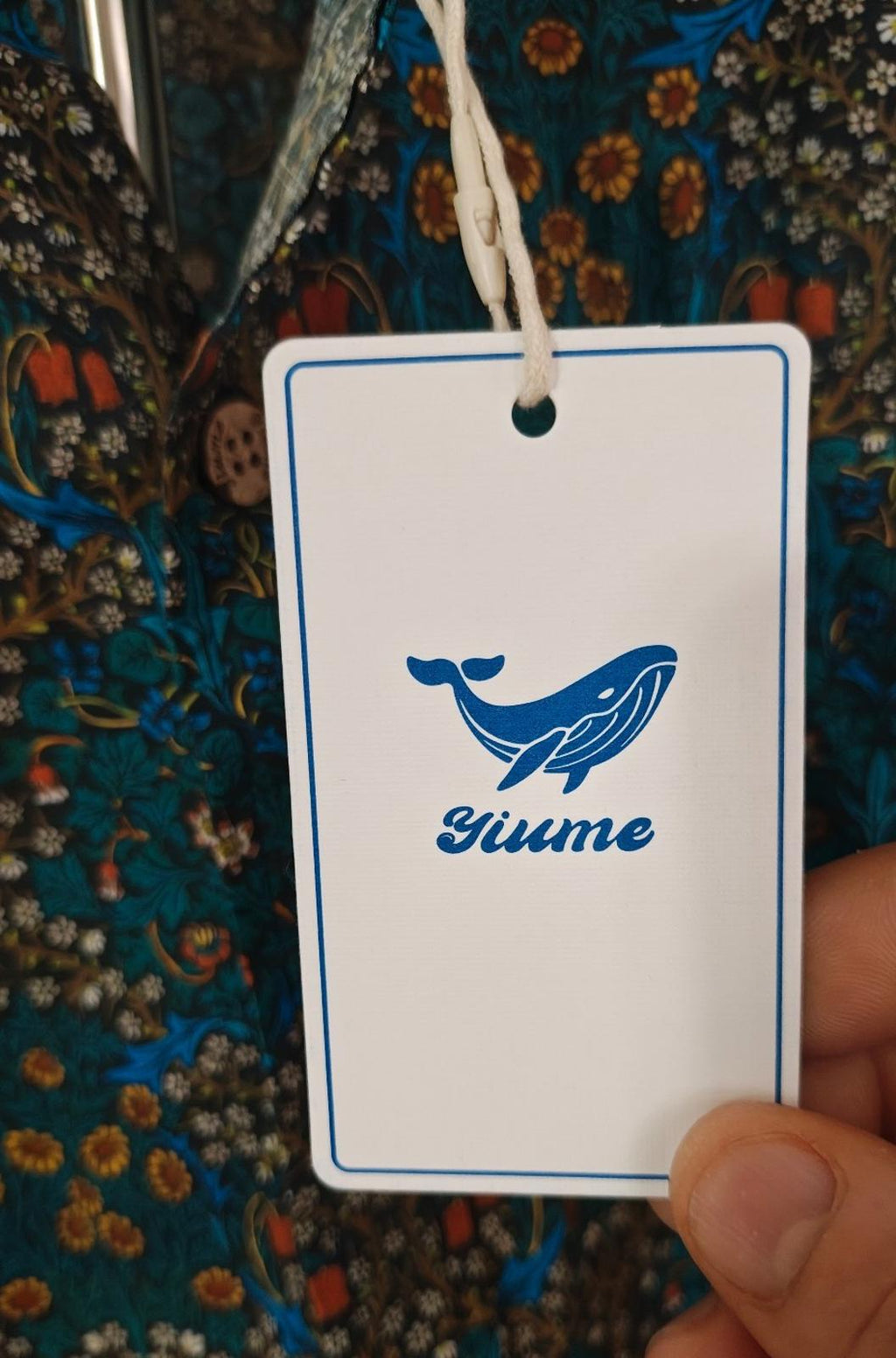 Blue floral Hawaiian shirt with white hang tag showing whale logo and Yiume branding