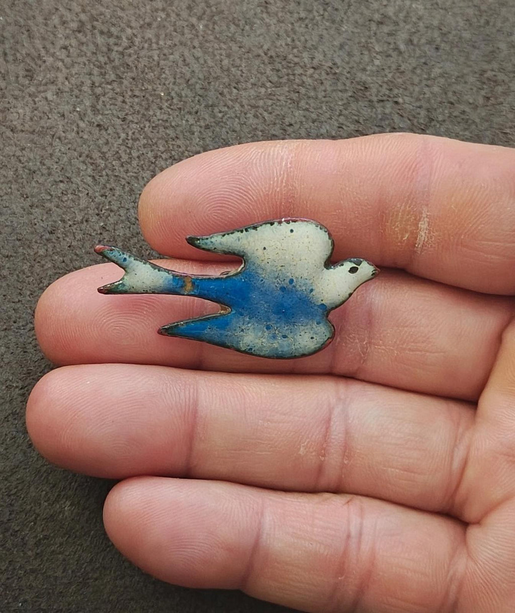 Blue and white enamel bird brooch in fingers, side view of wing tips