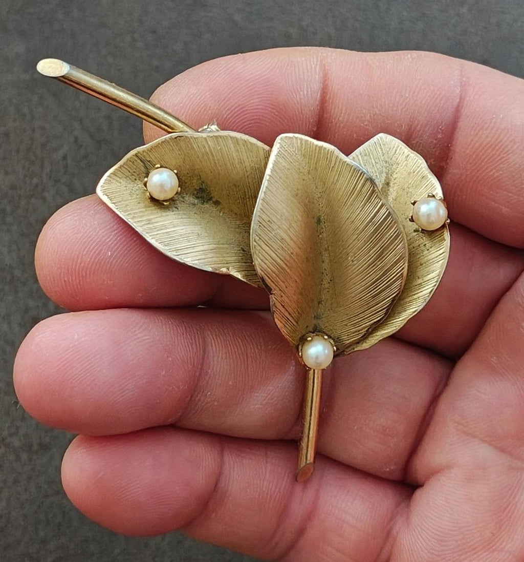 Gold leaf brooch close-up with textured petals and faux pearl accents on pin stem