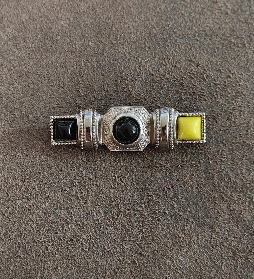 Small silver-tone bar pin brooch showing round dark cabochon with black square and yellow square