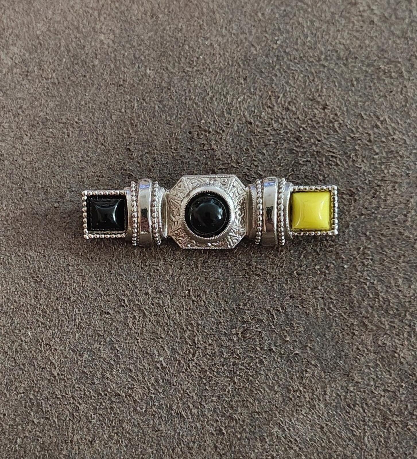 Small silver-tone bar pin brooch showing round dark cabochon with black square and yellow square