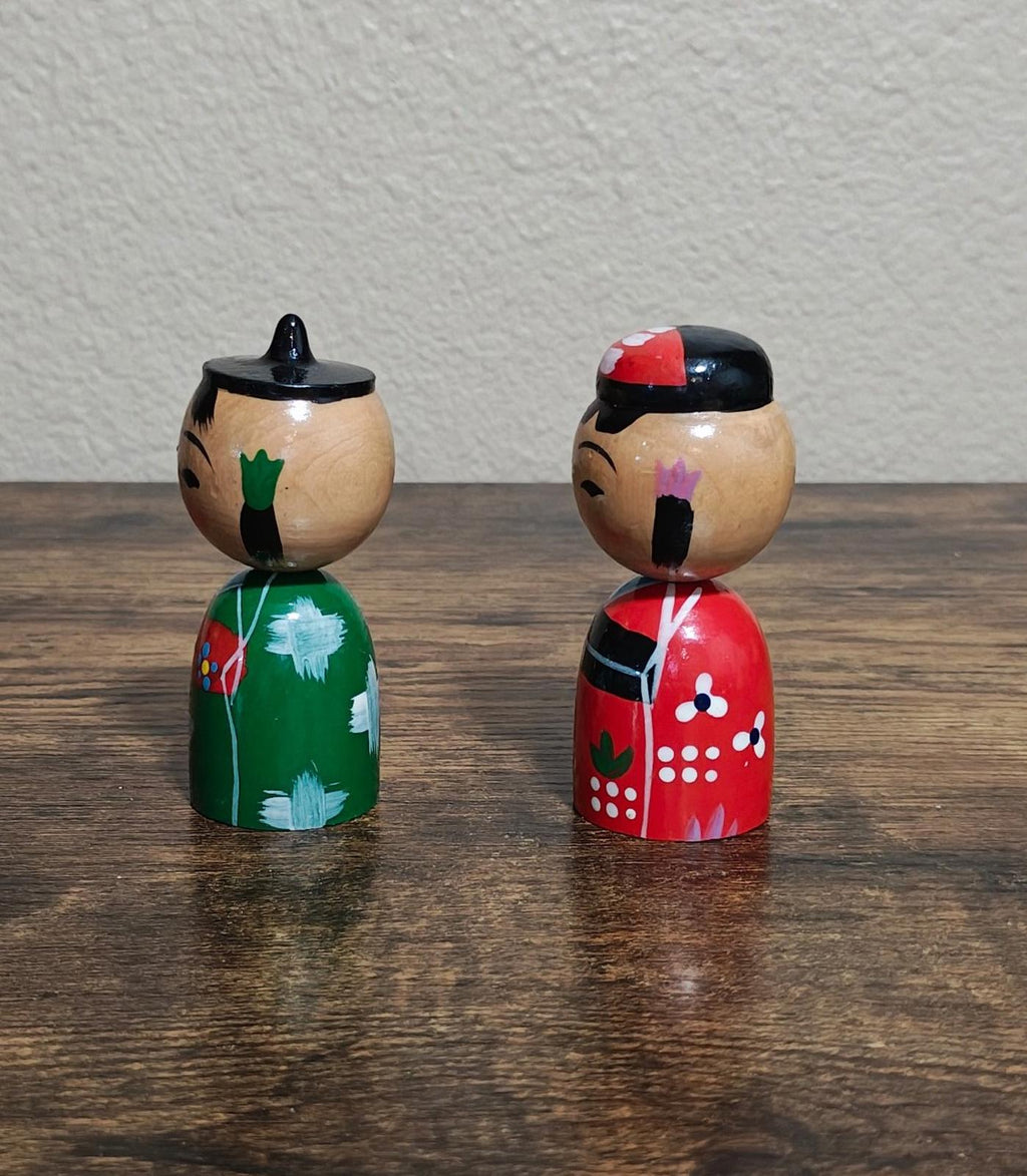 Pair of Japanese kokeshi wooden dolls viewed from the back, green and red dresses