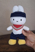 White bunny rabbit plush with navy farmer hat, red bandana bib, and yellow shoes.