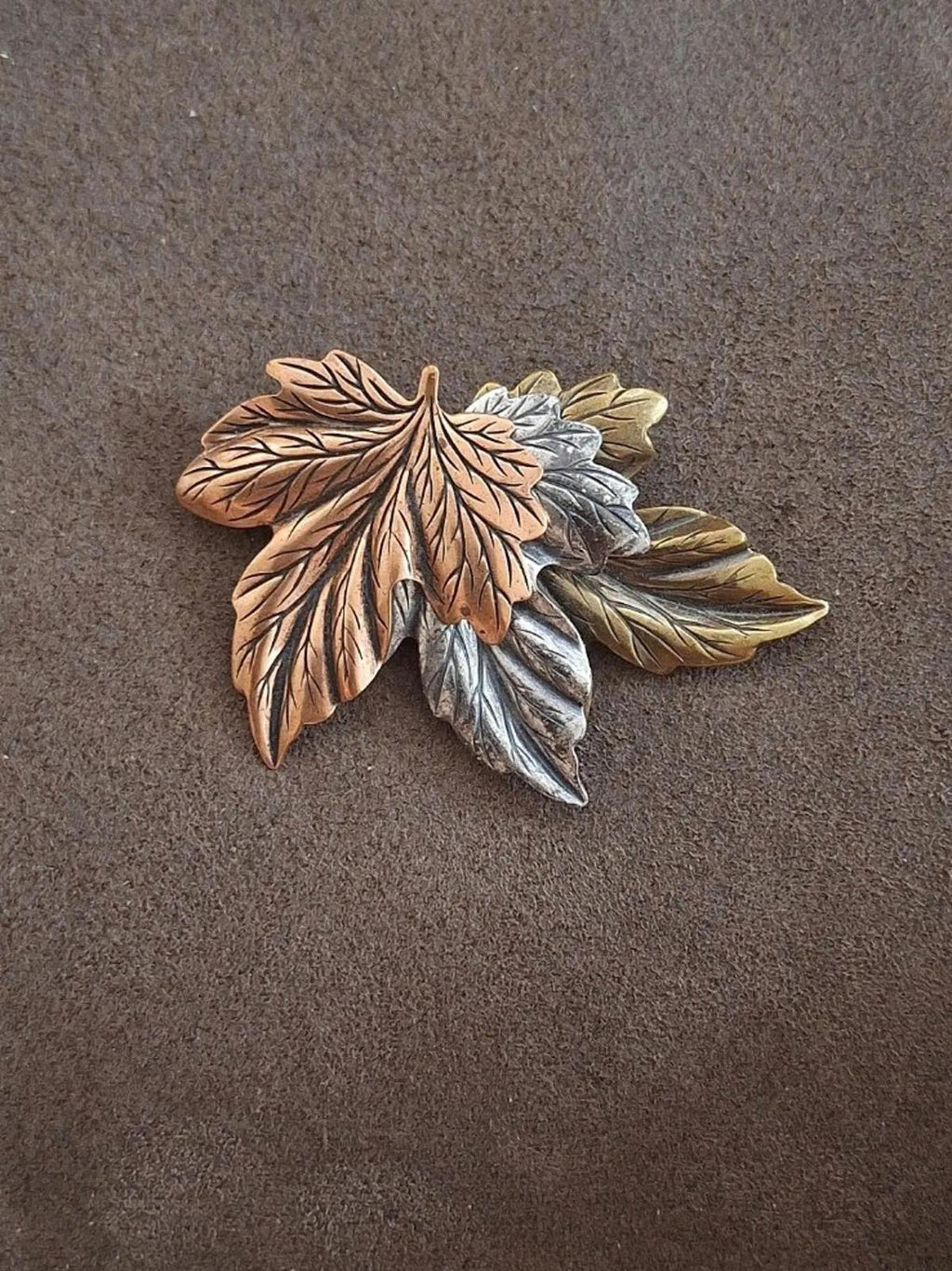 Layered leaf pin brooch with brown, gold, silver, and green-toned leaves on fabric