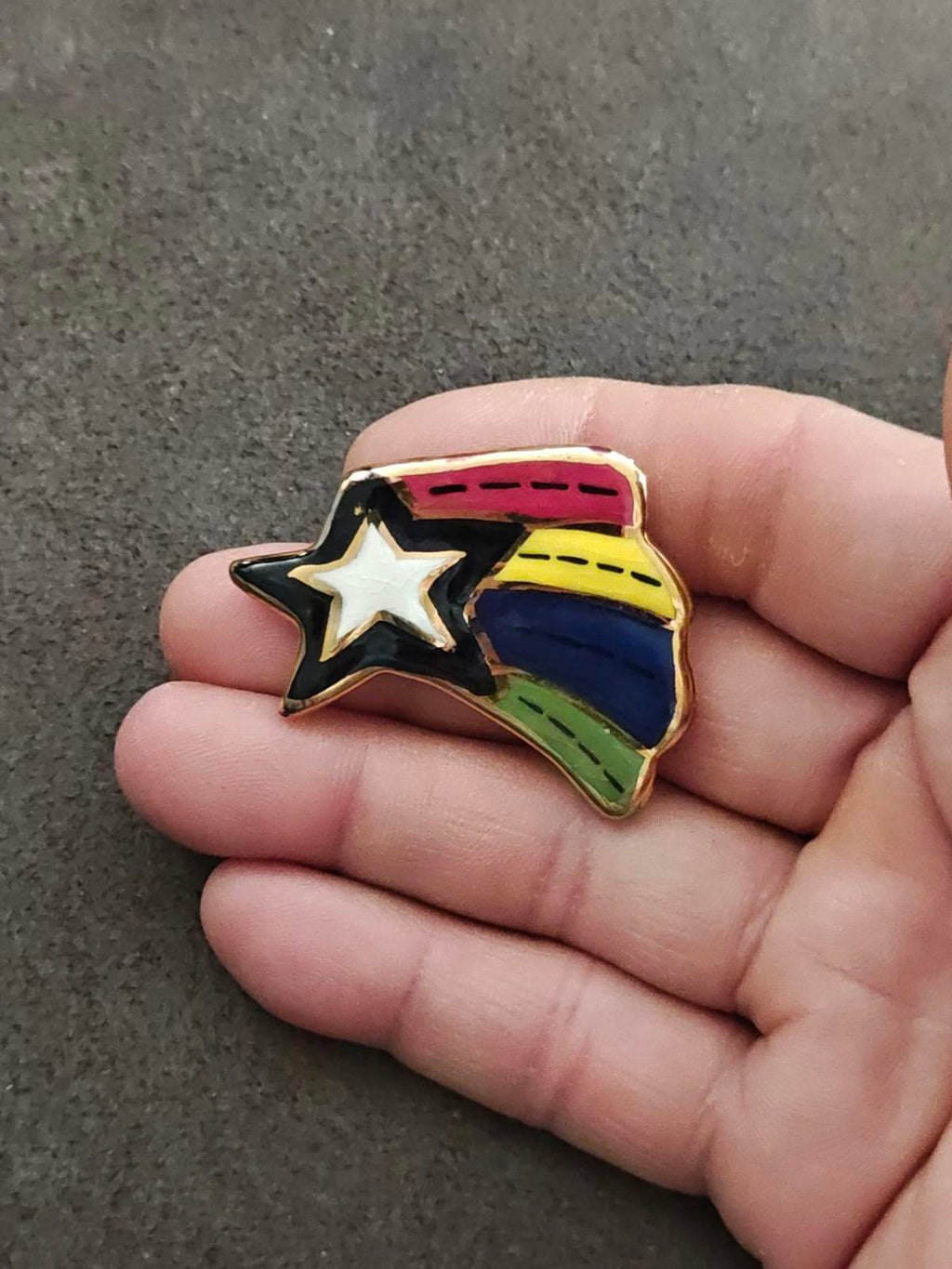 Glazed ceramic shooting star pin brooch with rainbow stripes and gold outline on hand