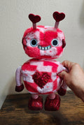 Red and white plush robot with heart sequin chest, big eyes, and heart antennae.