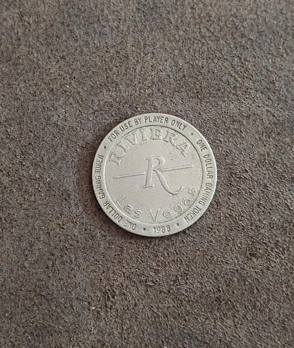 Silver one-dollar gaming token on floor with Riviera logo and 1988 date on rim
