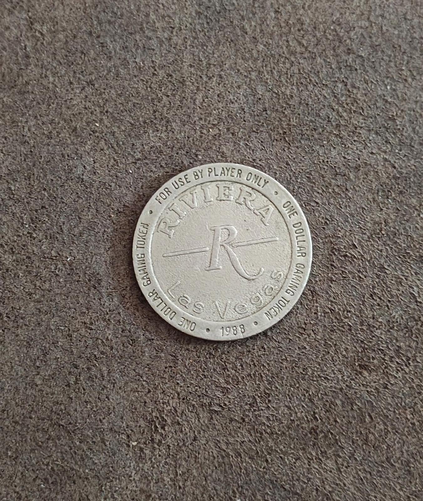 Silver one-dollar gaming token on floor with Riviera logo and 1988 date on rim