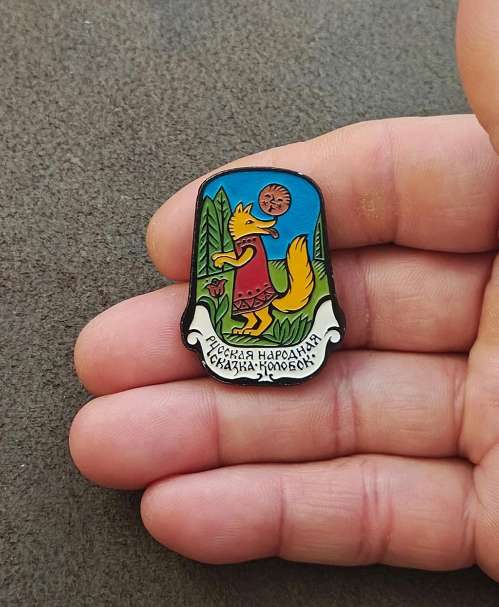 Children's Soviet enamel pin held in hand, blue fox and animal characters with lettering