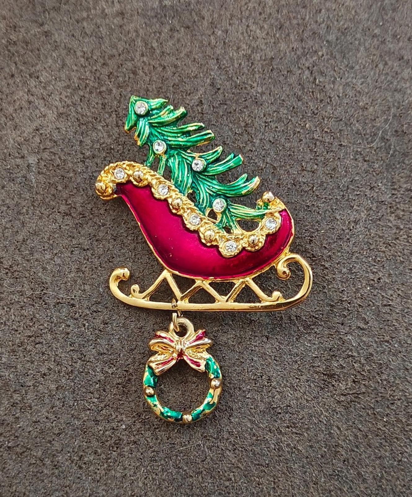 Gold and enamel sleigh pin with red enamel seat, green tree, and dangling wreath ornament.