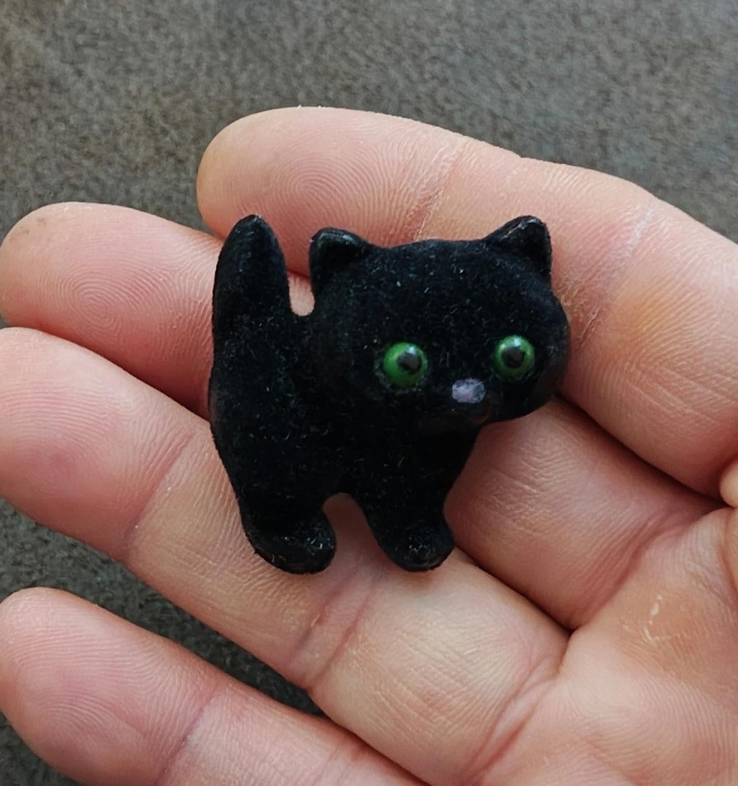 Black fuzzy cat brooch with green eyes held in hand