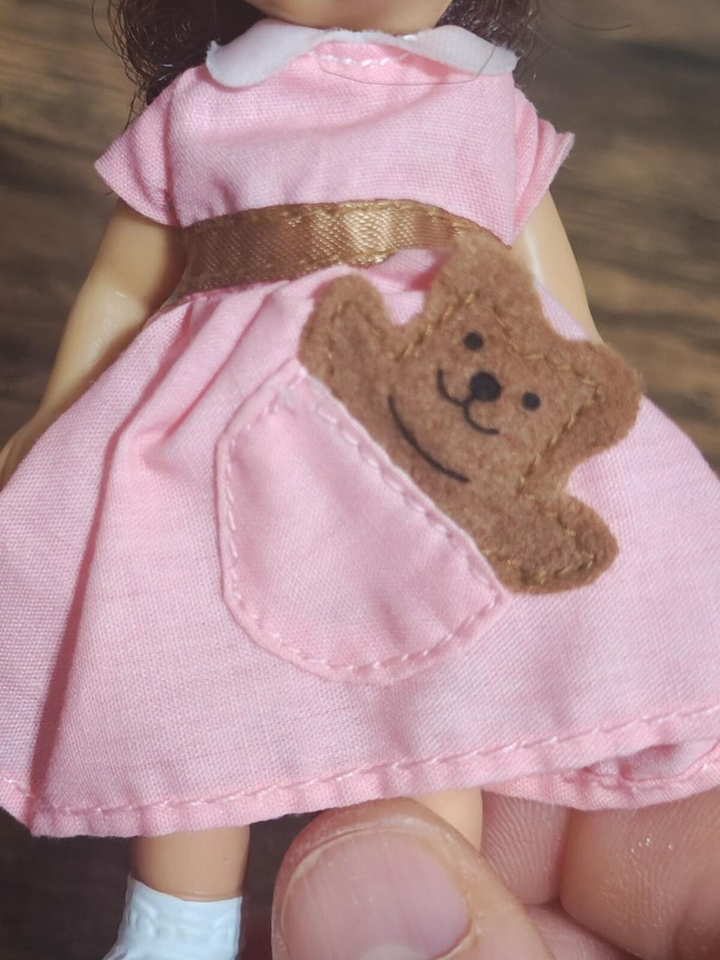 Close-up of pink doll dress with brown teddy bear applique and white pocket