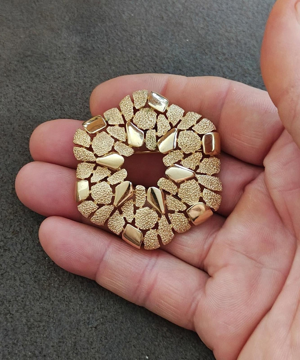 Gold-tone textured open-circle wreath brooch held in hand