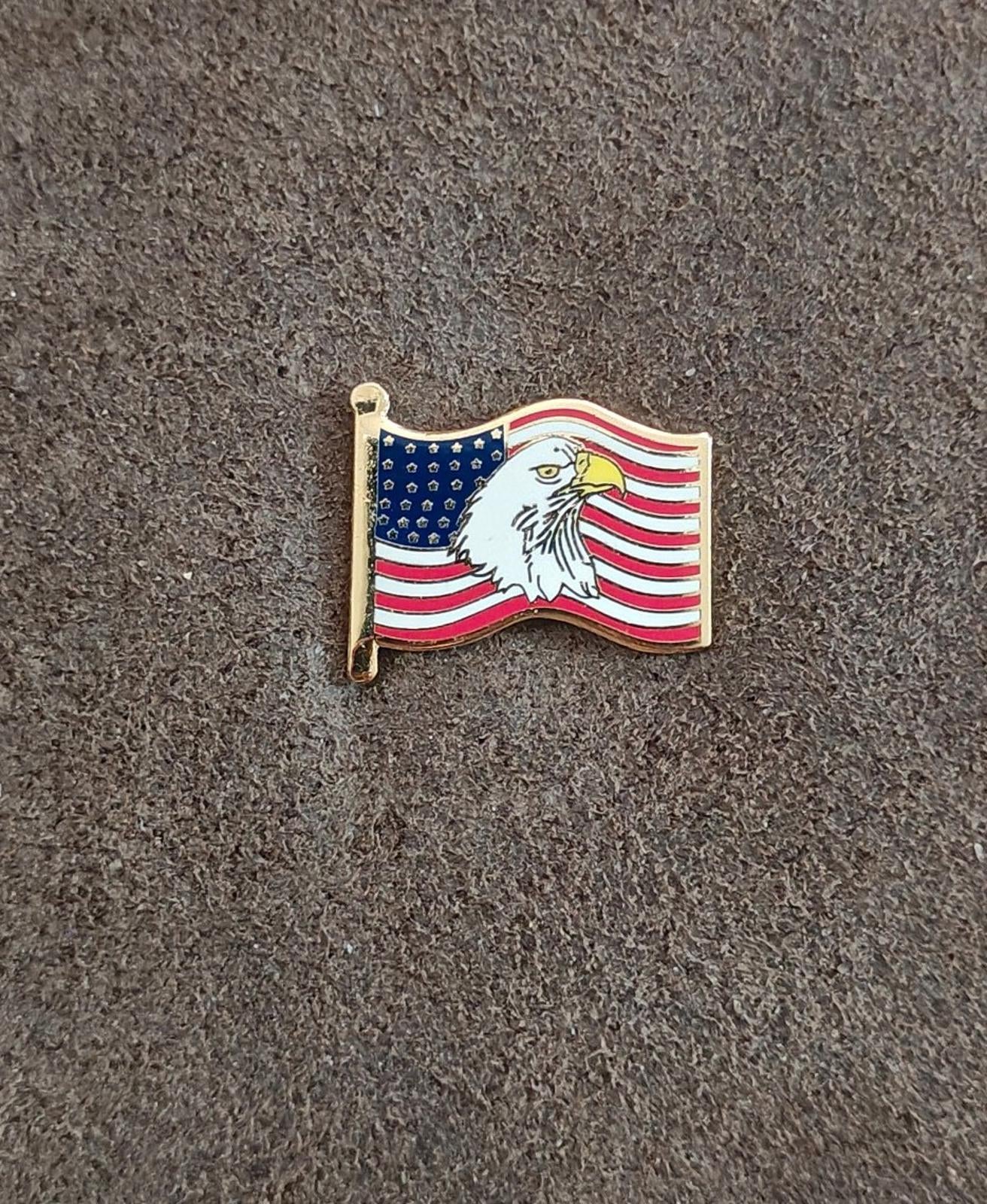 Gold-tone enamel wavy American flag lapel pin with bald eagle, laid on gray surface