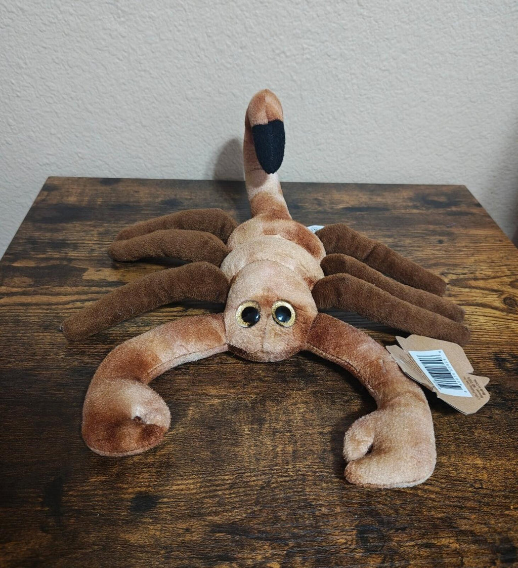 Brown plush scorpion with curled tail, floppy legs, and light tan face with blue eyes