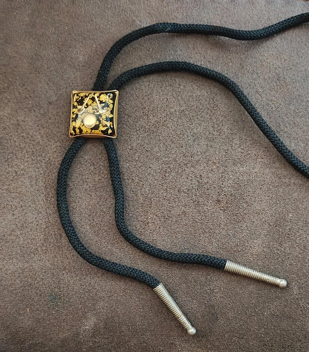 Black bolo tie cords with silver tips and gold square pendant featuring gold flecks