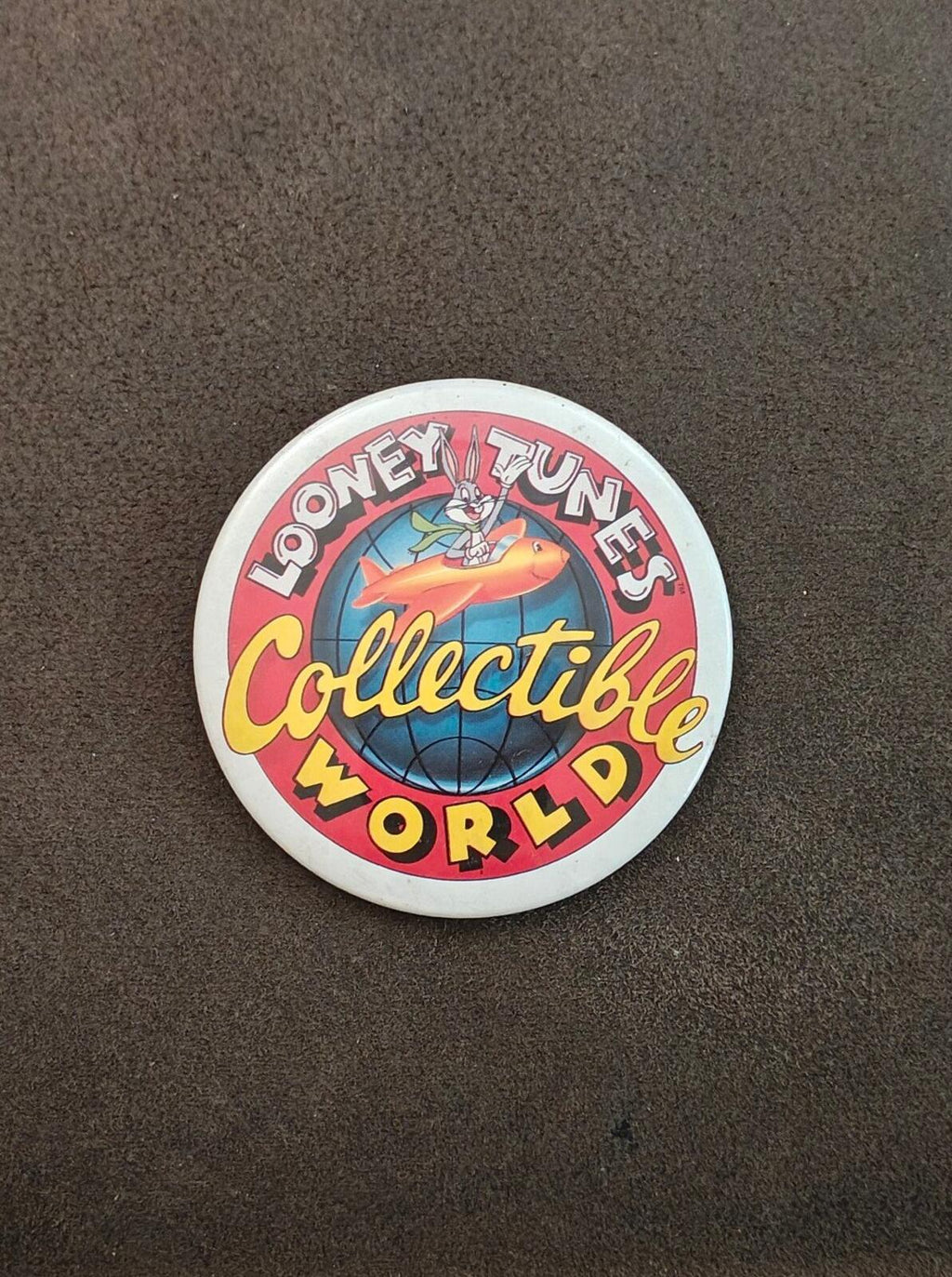 Round Looney Tunes “Collectible World” button pin with globe and rocket character artwork (small).
