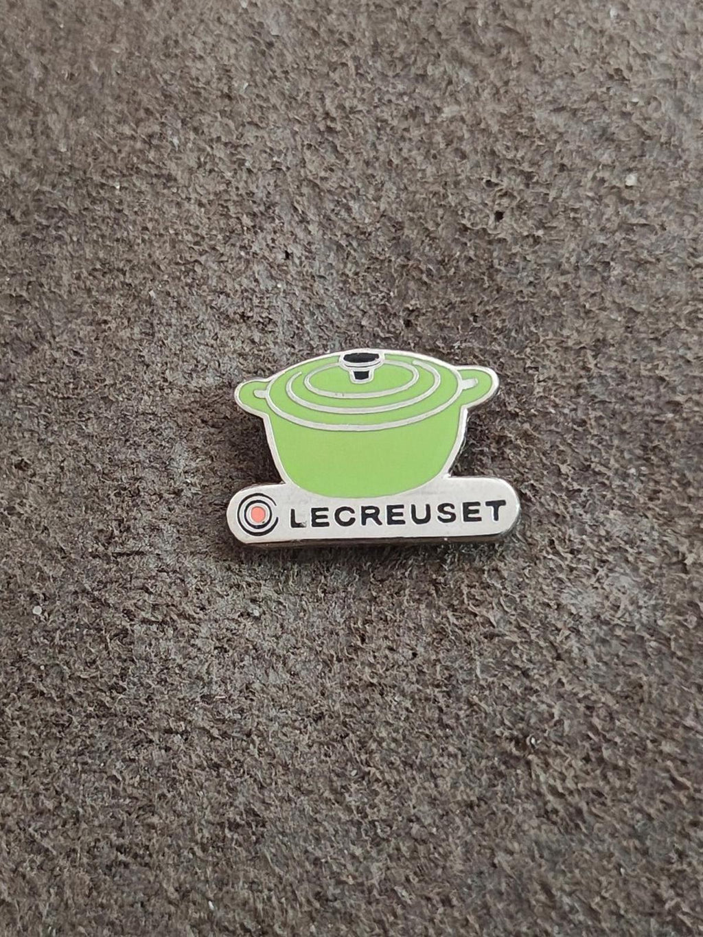 Le Creuset green mini cocotte enamel pin on gray fabric background