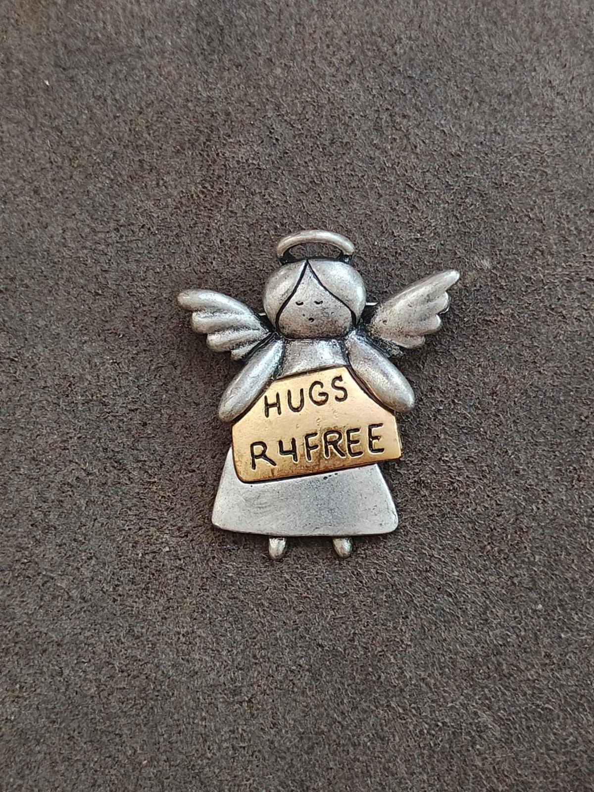 Silver winged angel charm brooch with tan sign reading HUGS R4FREE