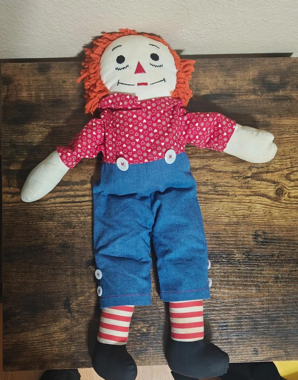 Handmade rag doll full body on display with orange yarn hair, red heart-pattern shirt, blue overalls.