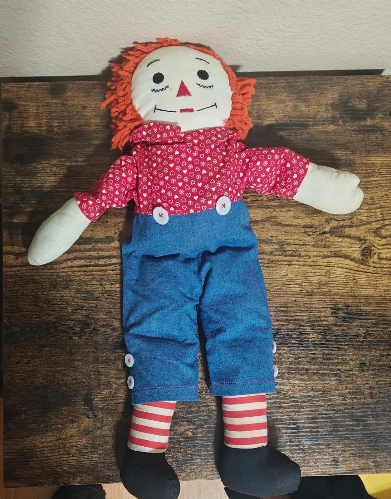 Handmade rag doll full body on display with orange yarn hair, red heart-pattern shirt, blue overalls.