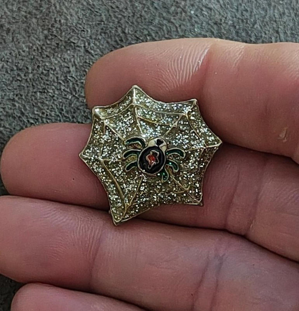 Gold glitter spider web enamel pin in hand, black spider with red center and green legs
