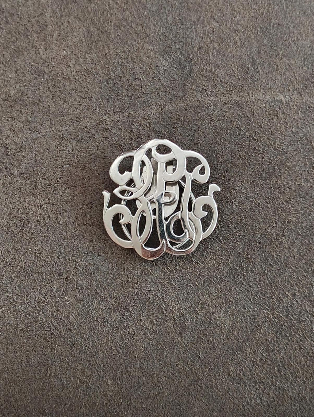 Silver-tone monogram scarf clip, front view on textured background