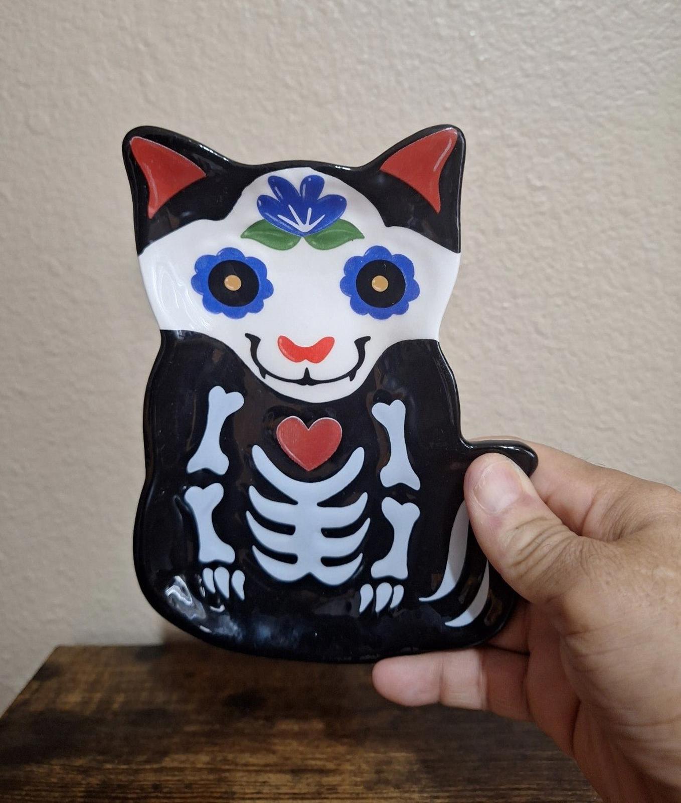 Black 3D cat sugar skull trinket plate held by hand; blue flowers and red heart center