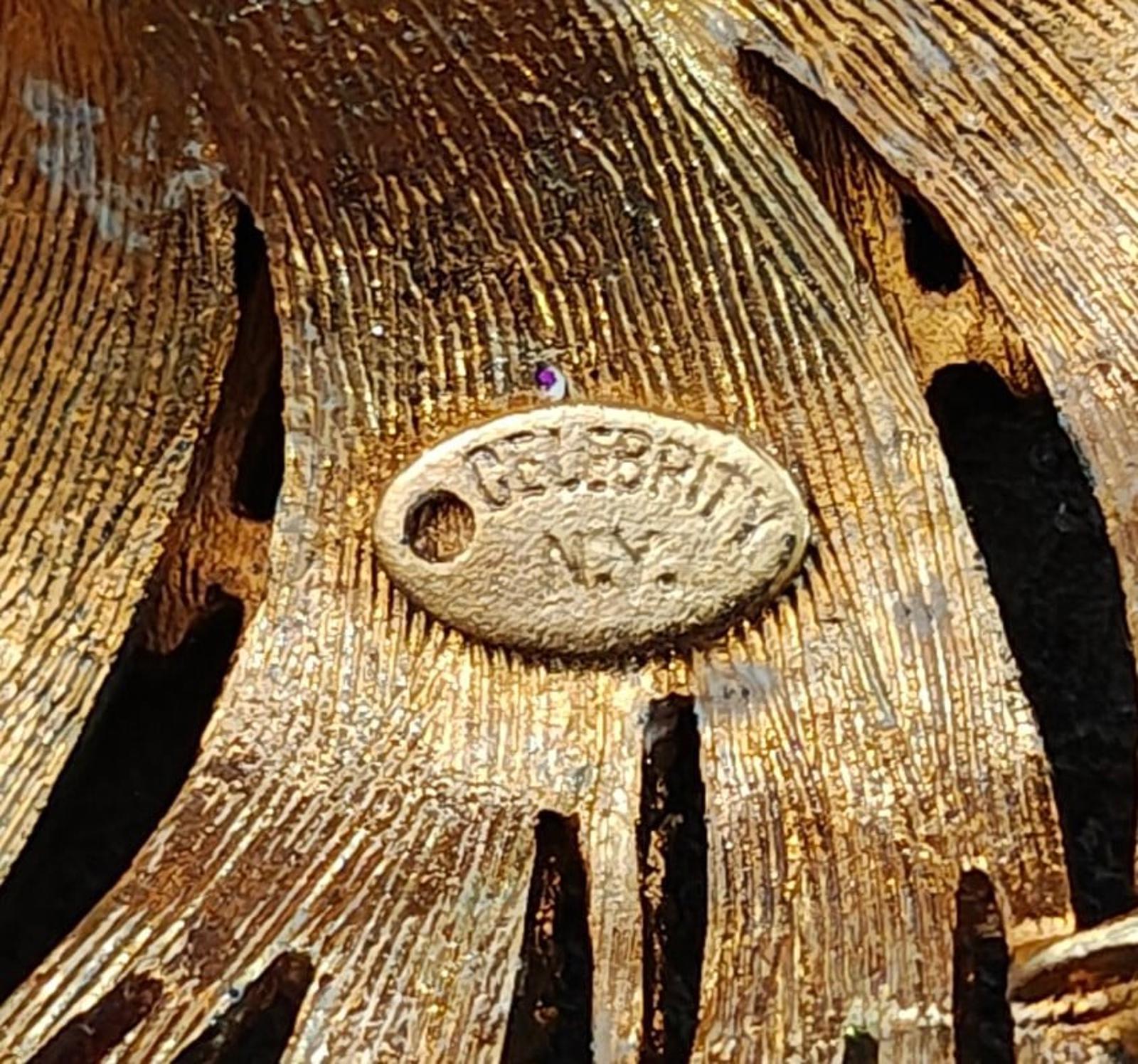 Gold-tone oval stamp on starburst brooch, with small purple accent detail