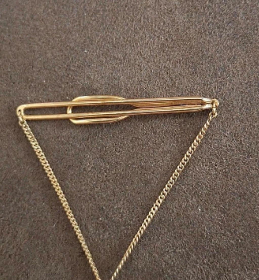 Gold-tone bowling-themed tie bar with long chain, laid flat.
