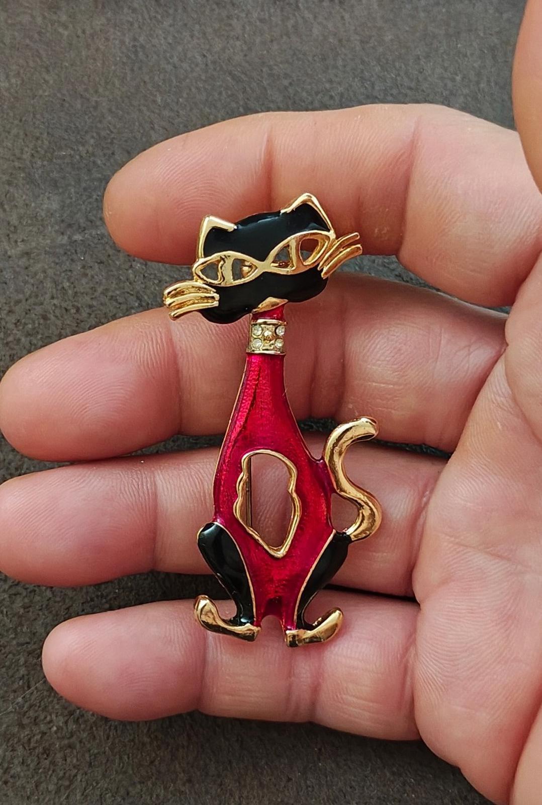 Red and black enamel cat mask brooch with gold-tone highlights, close view in hand.