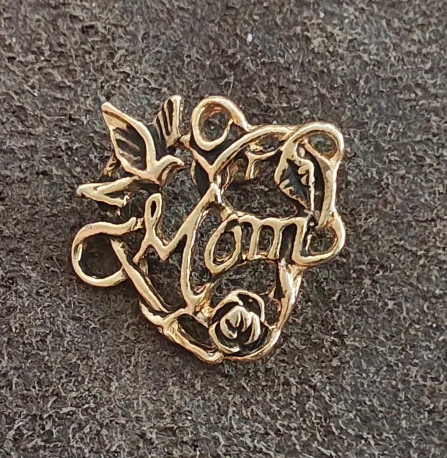 Gold-tone heart pin close-up with floral scrolls, rose, and “Mom” text