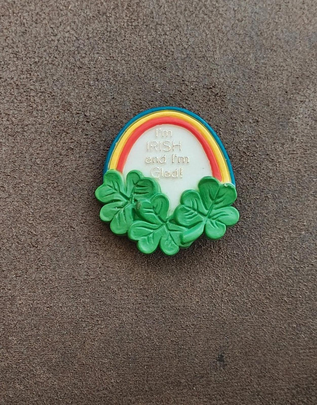 Green clover wreath rainbow brooch pin on gray surface, front view with embossed text
