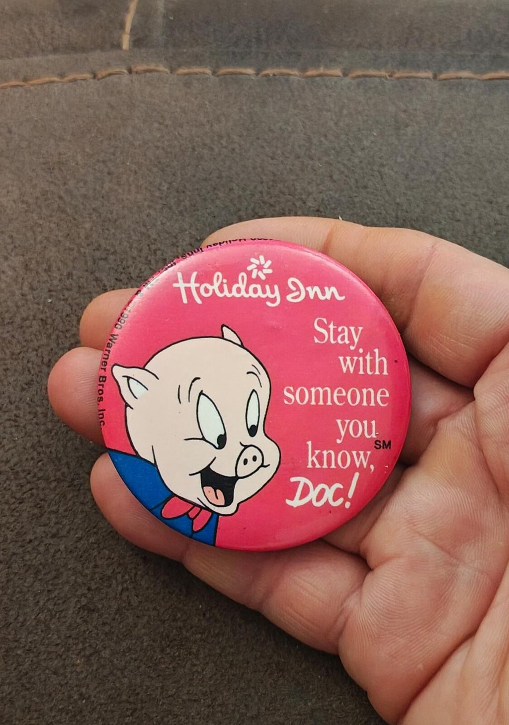 Pink button pin held in hand with Porky Pig and holiday message text