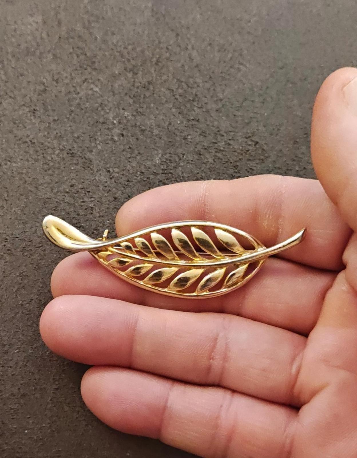 Gold tone leaf brooch with openwork filigree feather motif, held in hand