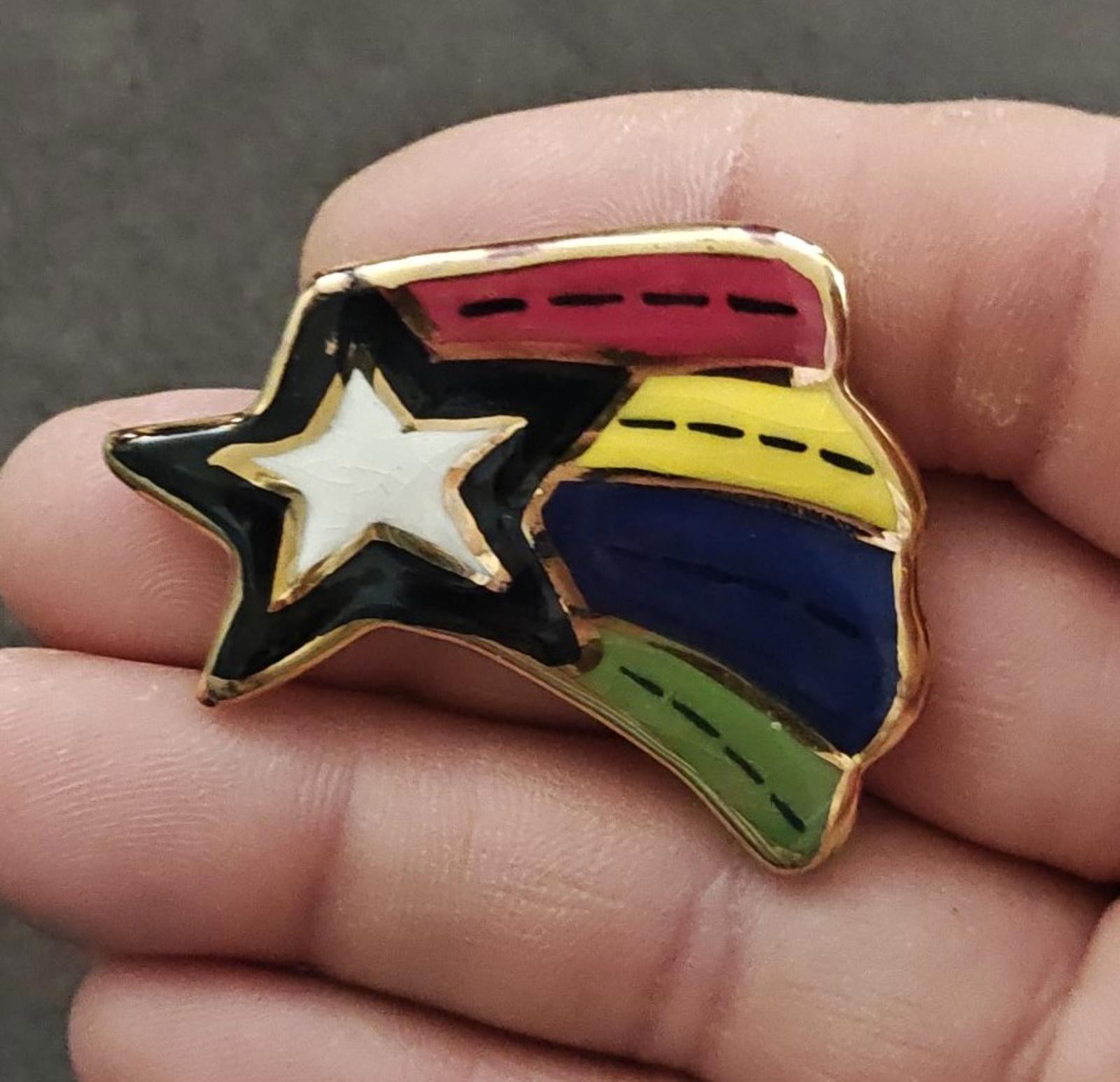 Close-up of glazed ceramic shooting star pin brooch with rainbow stripes and white star