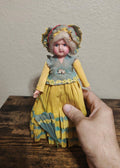 Handcrafted crepe paper doll with yellow layered dress and blue ruffle trim, held upright