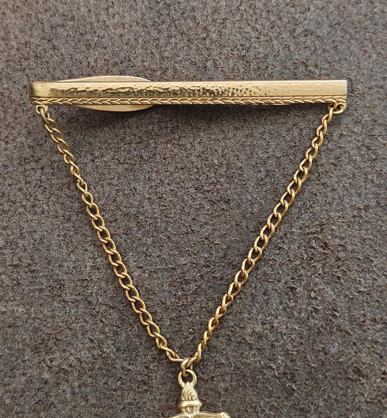 Gold-tone tie clip with chain and book charm marked 49, top view