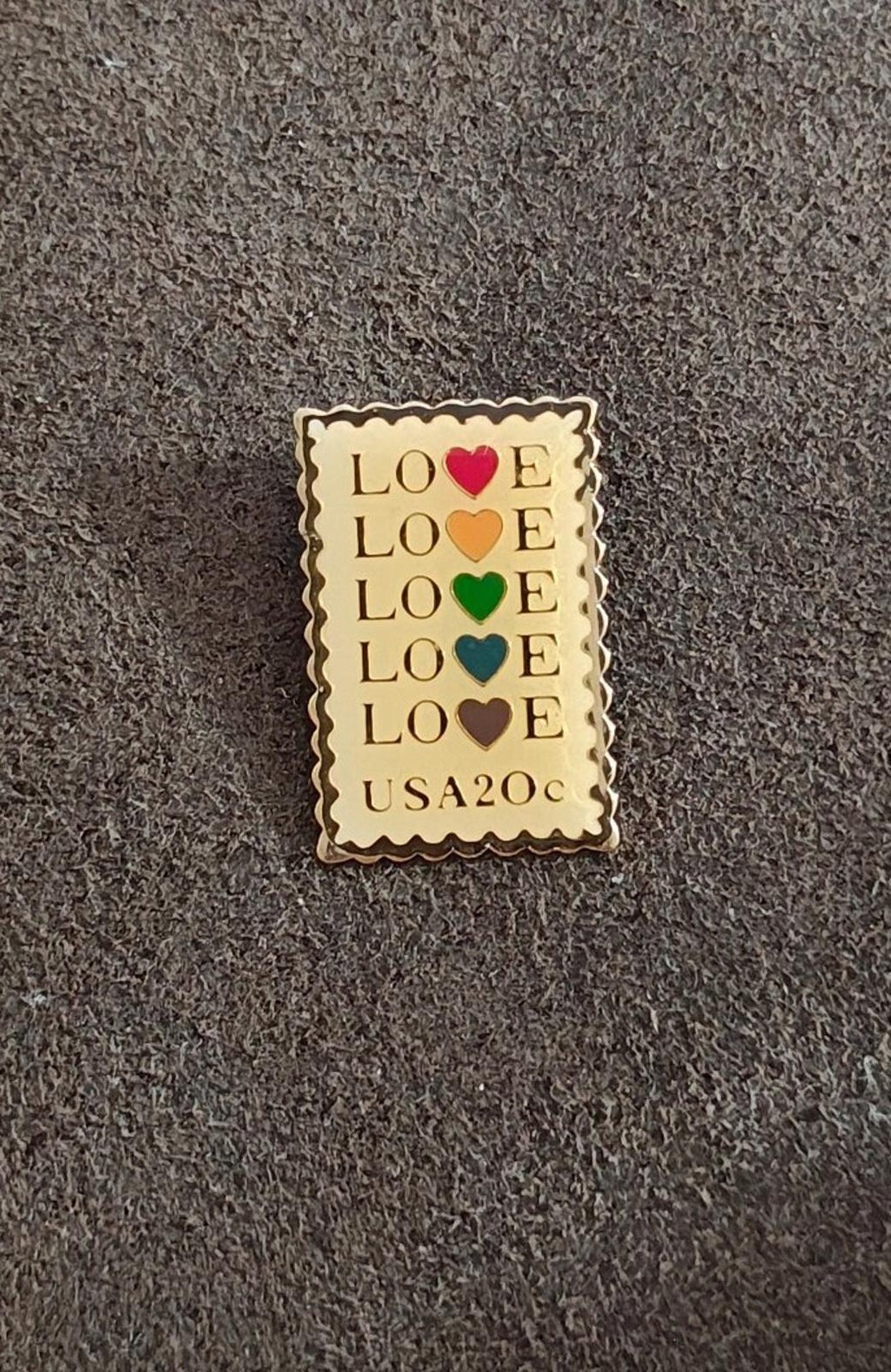 Gold-tone enamel pin with scalloped border and stacked “LOVE” hearts; “USA20c” visible.