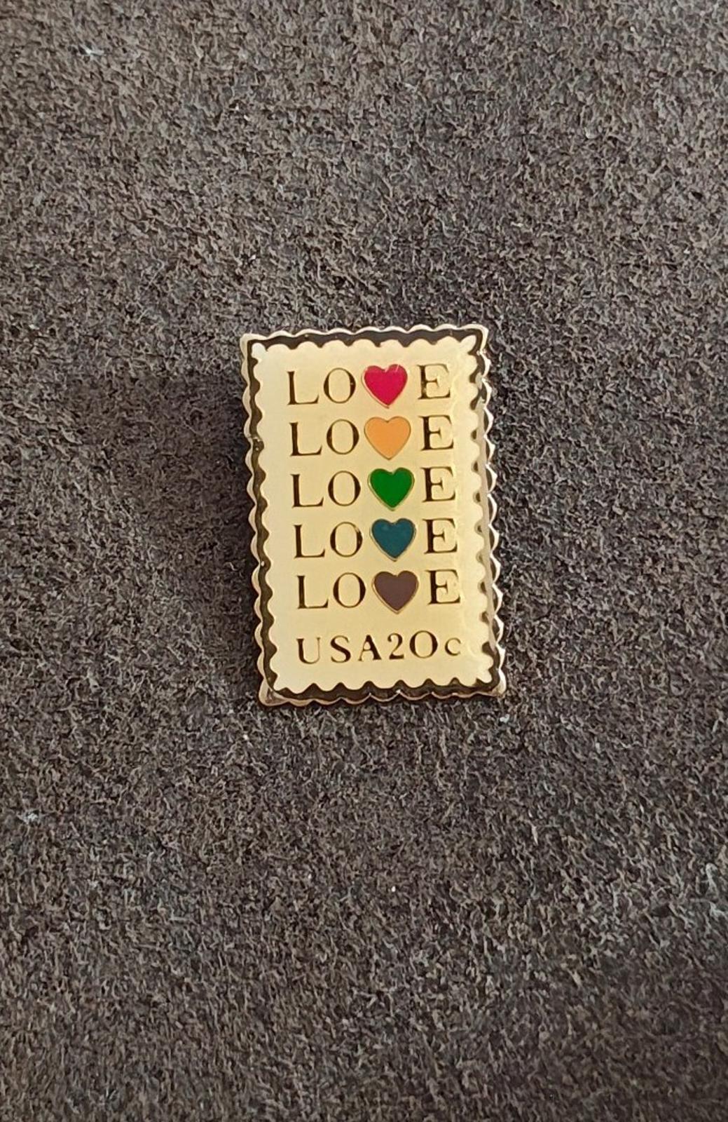 Gold-tone enamel pin with scalloped border and stacked “LOVE” hearts; “USA20c” visible.