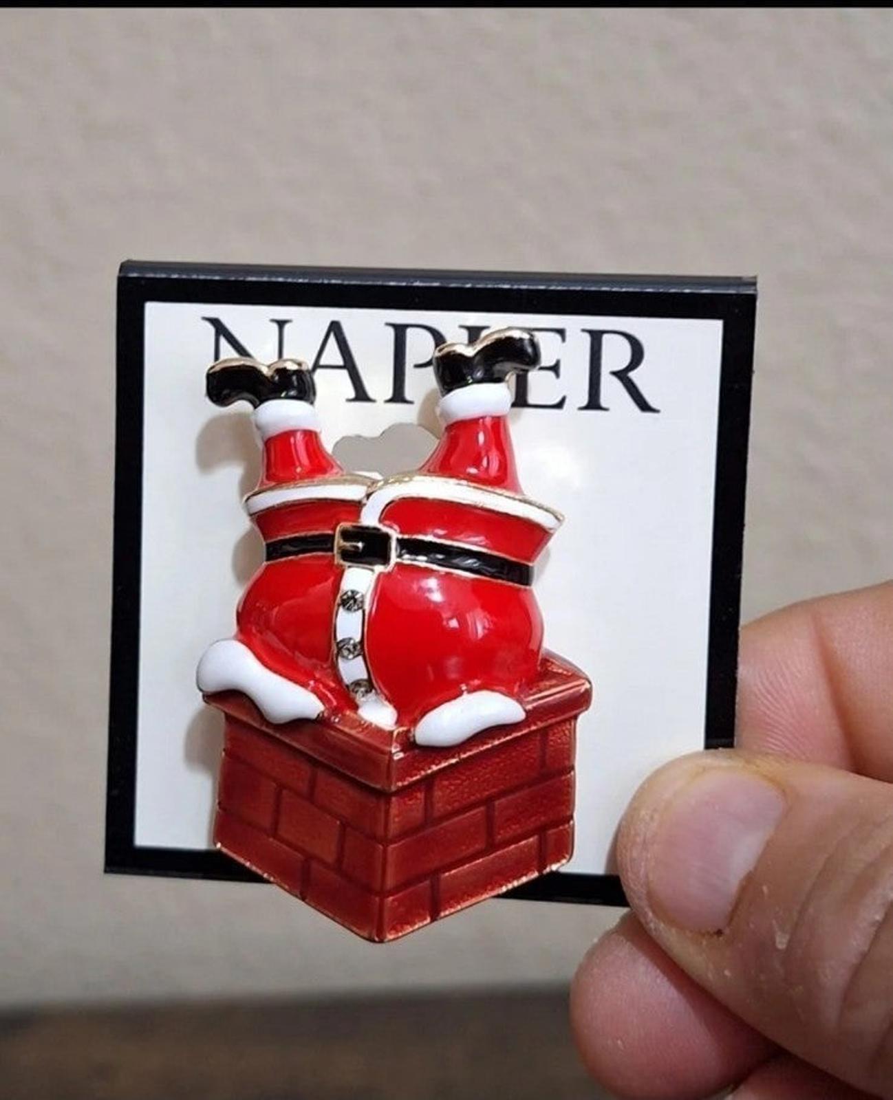 Red enamel Santa climbing down chimney pin on card, close-up with holding finger