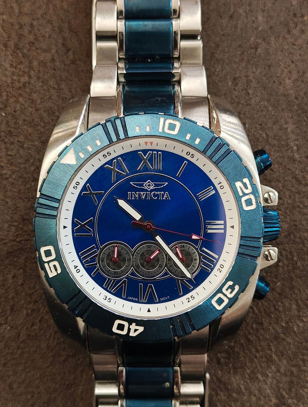 Men's blue Invicta chronograph watch face with roman numerals and three subdials