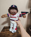 Baseball uniform doll with dark blue helmet and white Angels jersey, holding bat