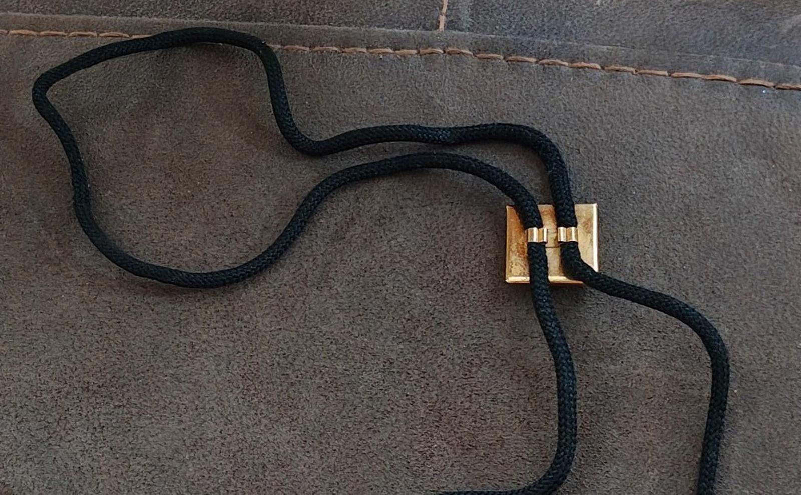 Back view of black bolo tie showing gold clasp at cord ends