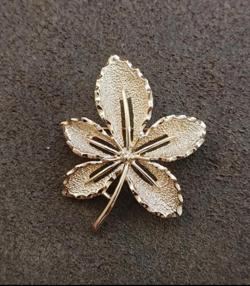 Gold-tone leaf flower brooch on dark background; five petals with central stem